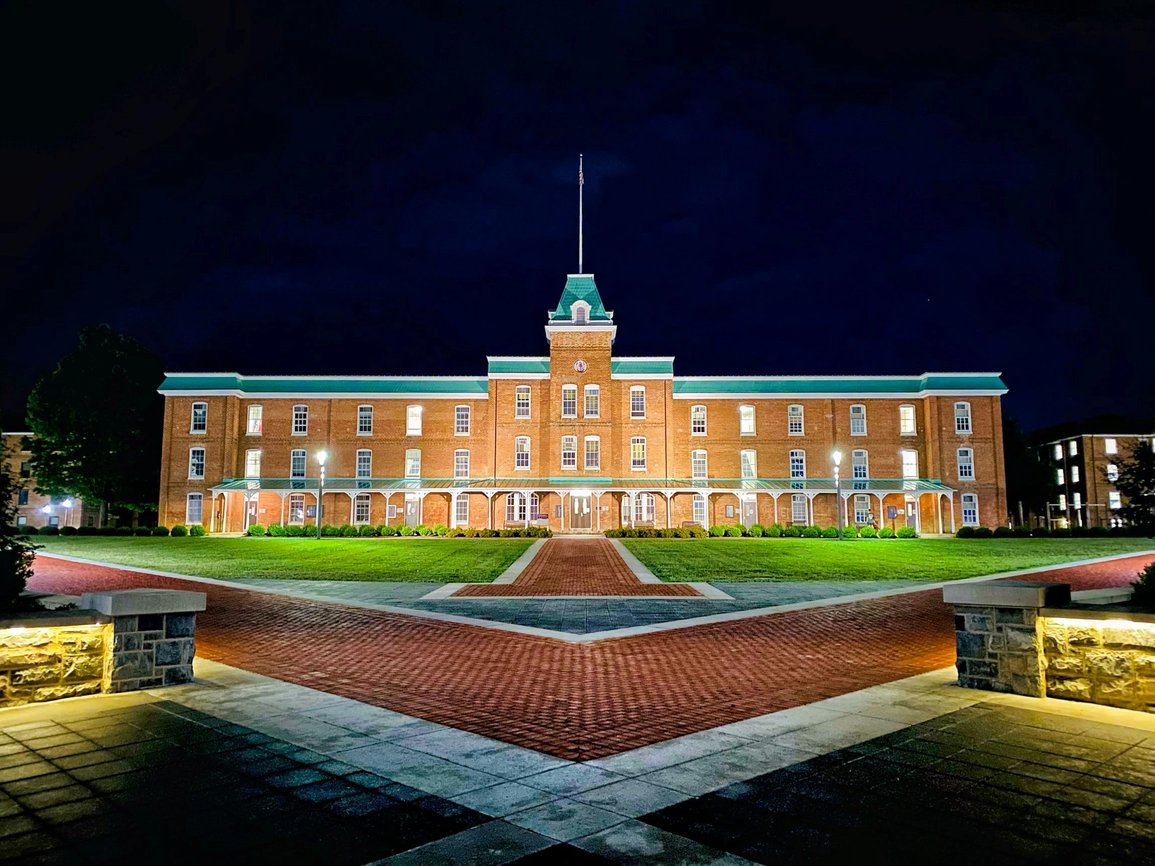 A university campus building lit at night beneath an American flag